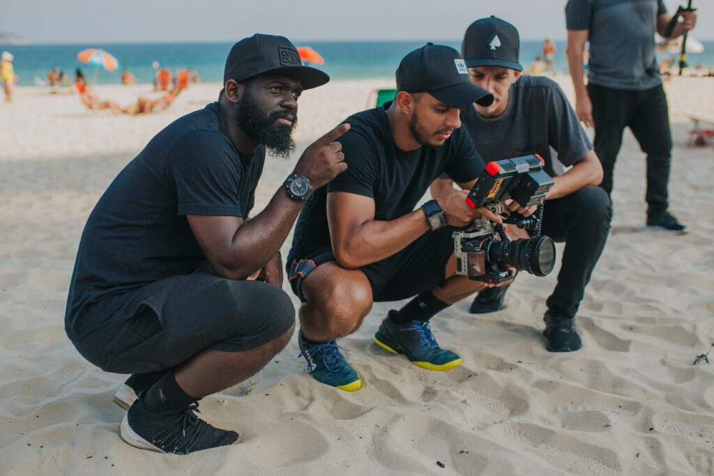 photo of of three men on a beach as part of a production crew for film or TV